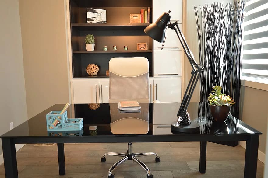 A DIY home office with a glass desk and a lamp.