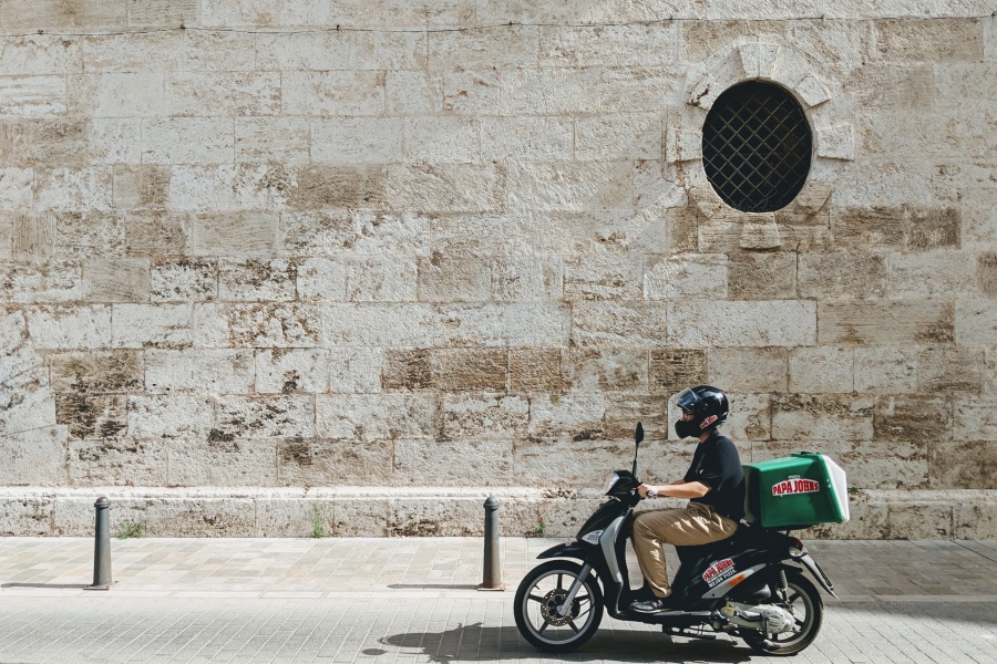 A man using a scooter to deliver a pizza.