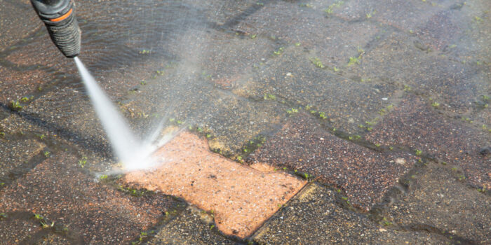 A man using a pressure washer to clean a brick walkway regularly.