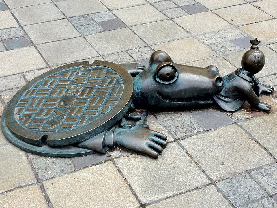 An interesting statue of a frog on a sidewalk.