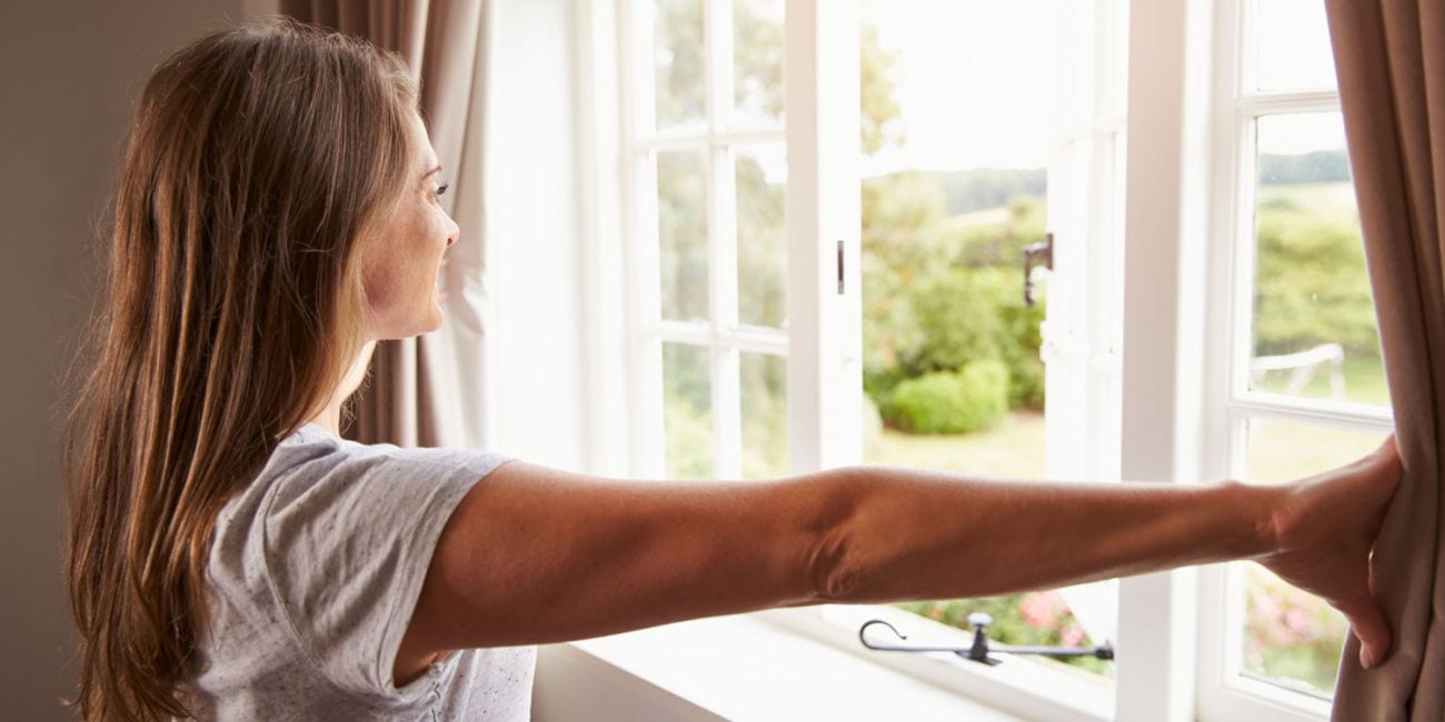 Easy ways to improve your home air quality with a woman opening a window.