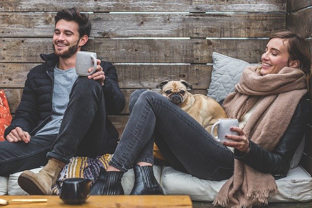 A couple sitting on a wooden bench with a dog and cup of coffee in their winter-friendly outdoor living space.
