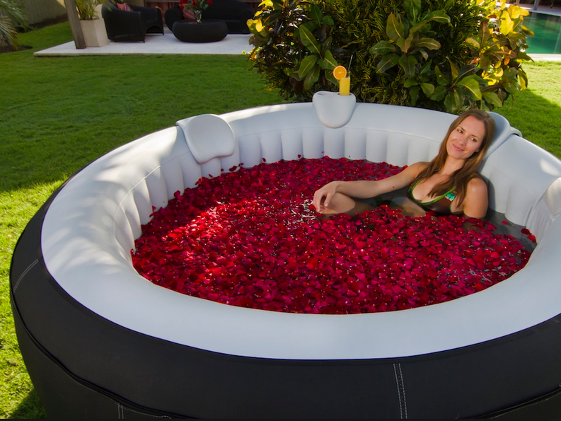 A woman is sitting in an inflatable hot tub filled with rose petals, enjoying the 5 benefits of having an Inflatable Jacuzzi Tub.