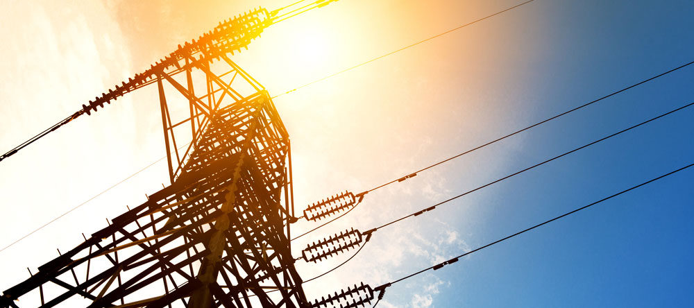 A high voltage pylon towering with the sun behind it, showcasing the expertise of an electrical contractor.