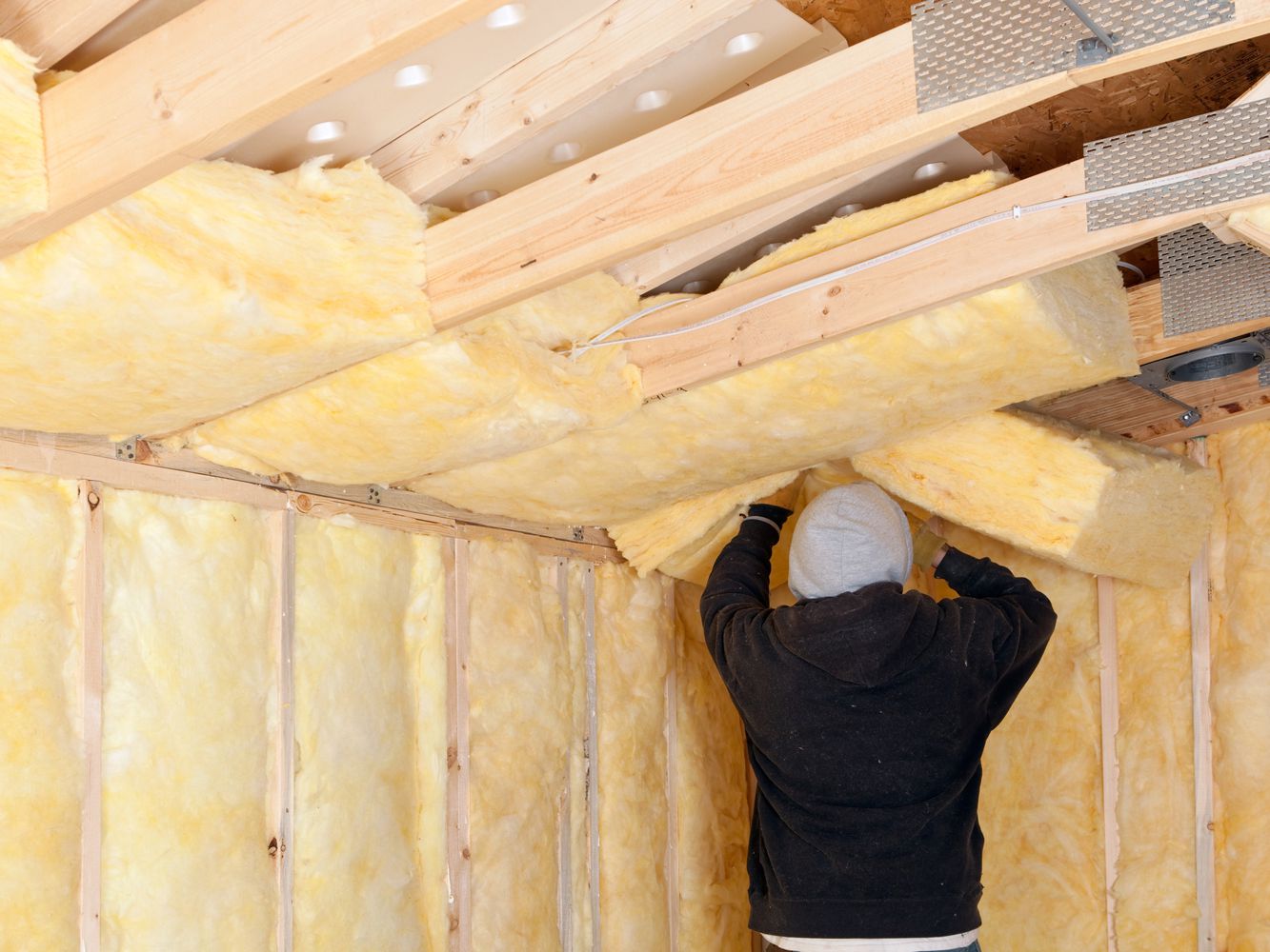 A man installing faced insulation batts in a room.