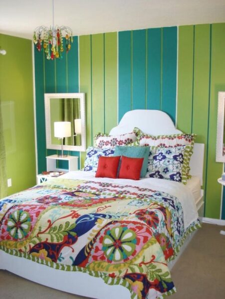A boho bedroom with green walls and a colorful bed.