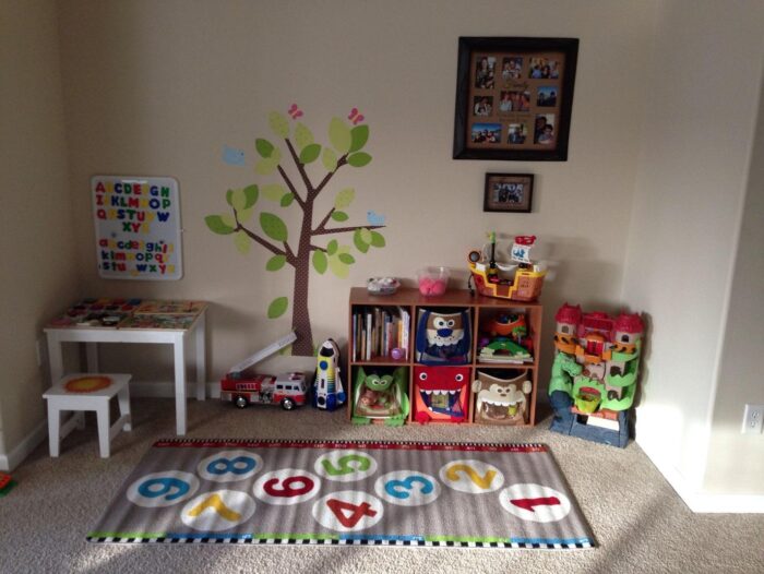 A kids’ room with toys and a tree on the wall.