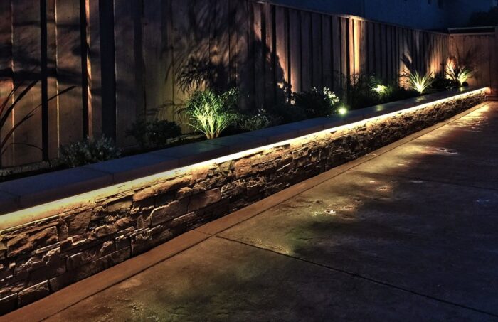 A backyard with a stone wall and LED lighting.
