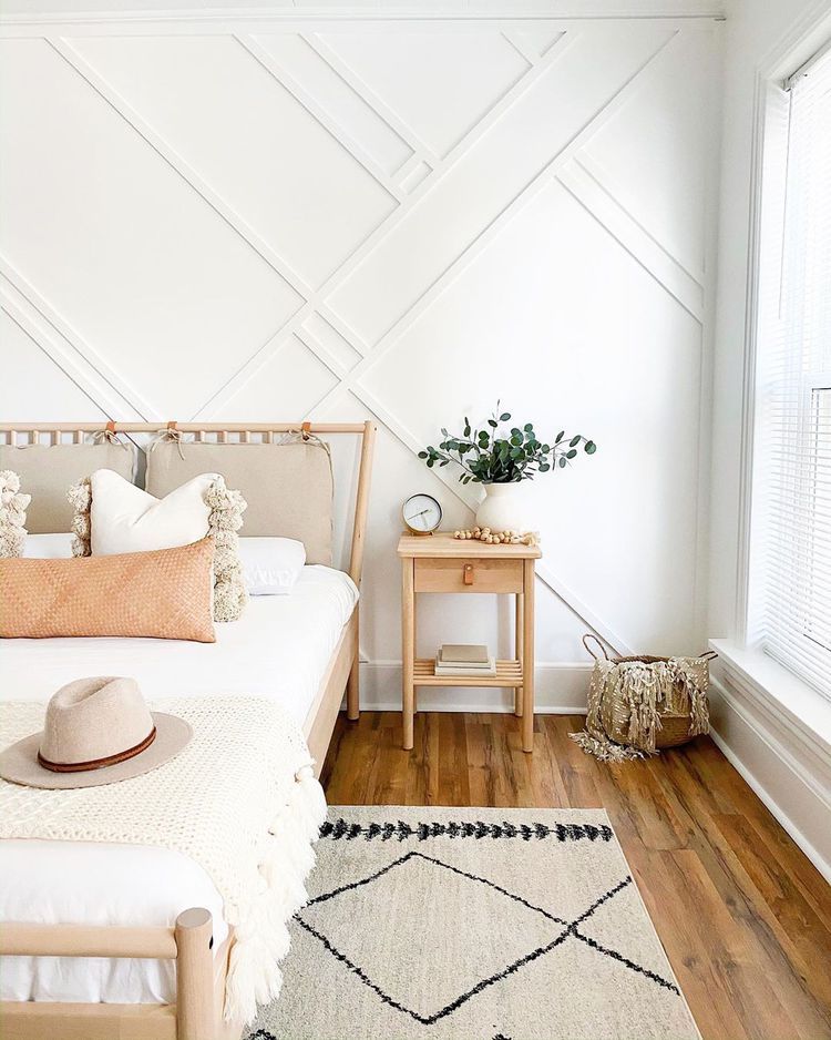 A white bedroom with wood floors, a bed, and a nightstand.