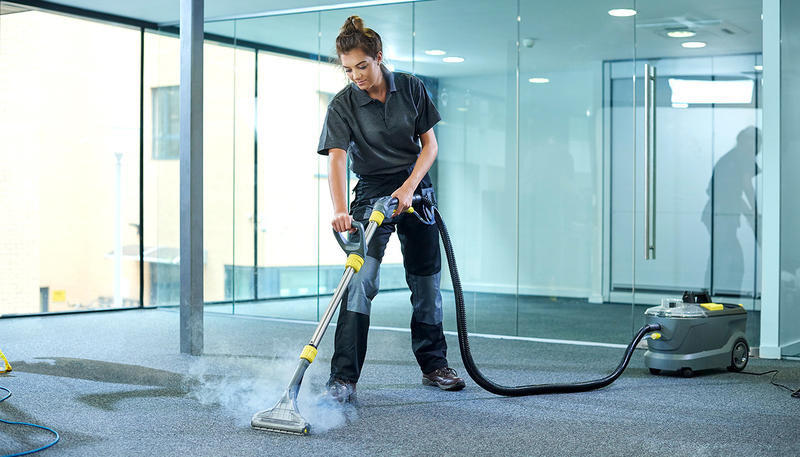 A woman cleaning carpet tiles in an office.