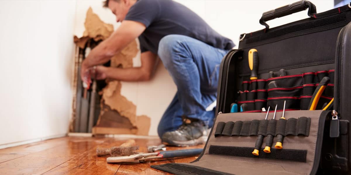 A man is performing home maintenance on a broken floor with tools.