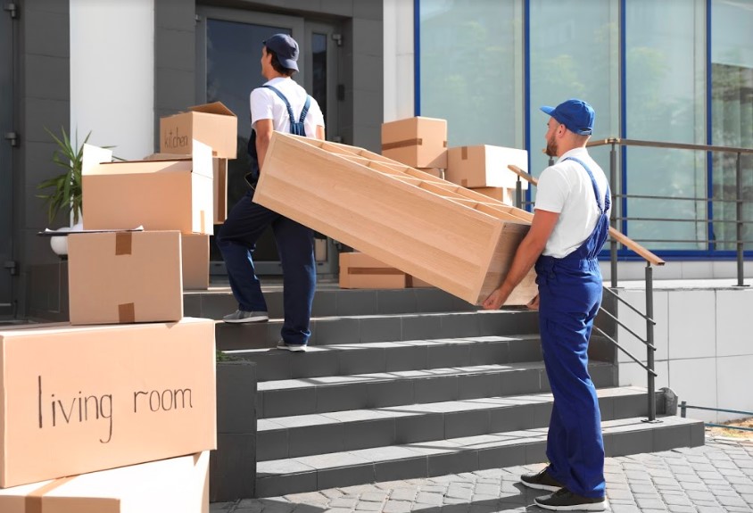 Two men moving boxes on the steps of a building.