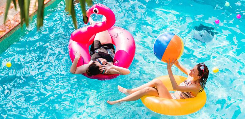 Two women are floating in a family pool with inflatable flamingos.