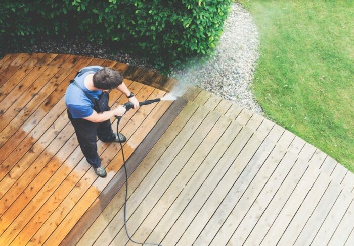 A man pressure washing a wooden deck at home.