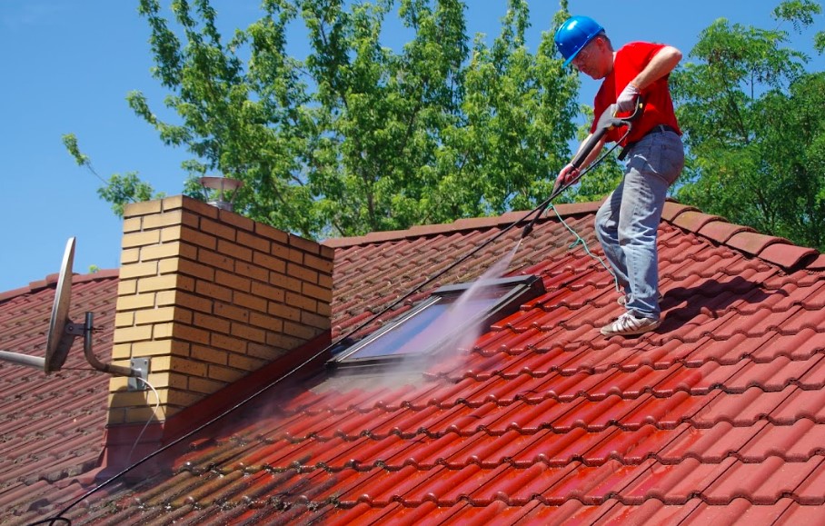 A man pressure washing a red tile roof.