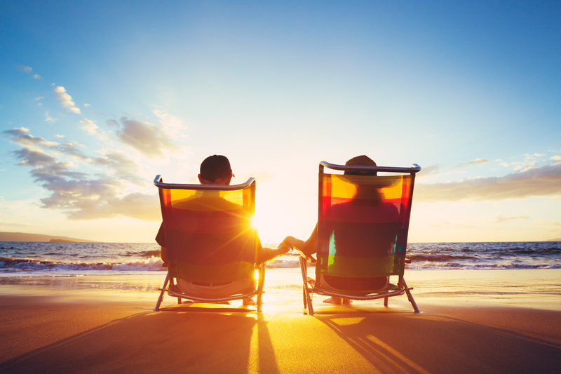Two people comfortably sitting in chairs on the beach at sunset.