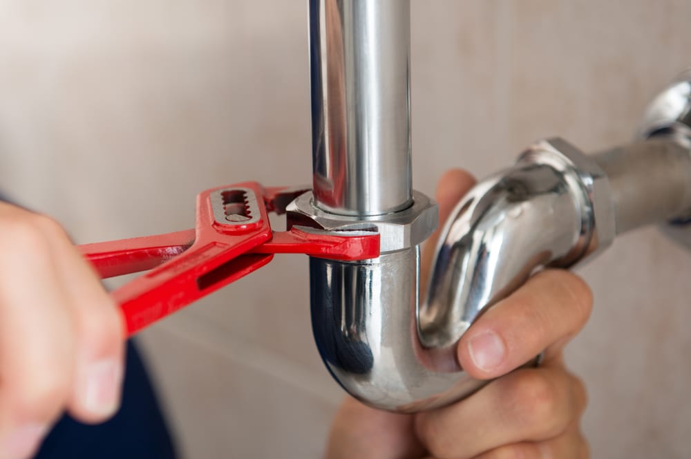 A man is performing plumbing repairs with a pair of pliers.
