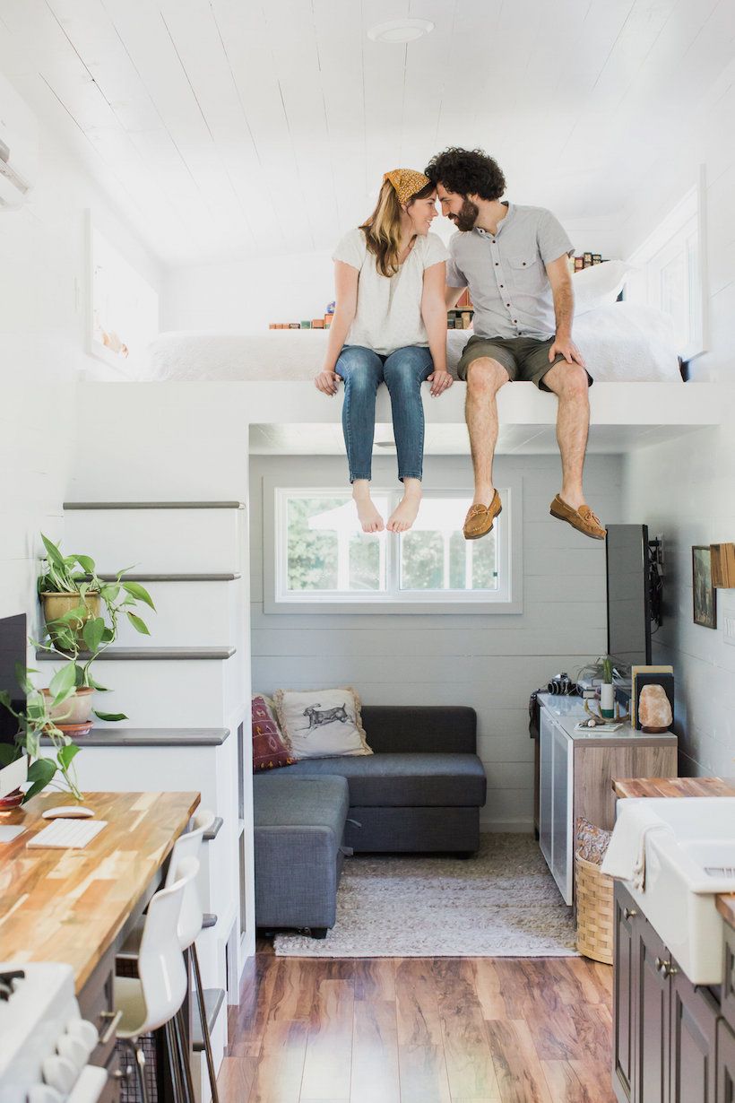 A couple sitting on top of a loft in a tiny house furnished with cozy furniture.