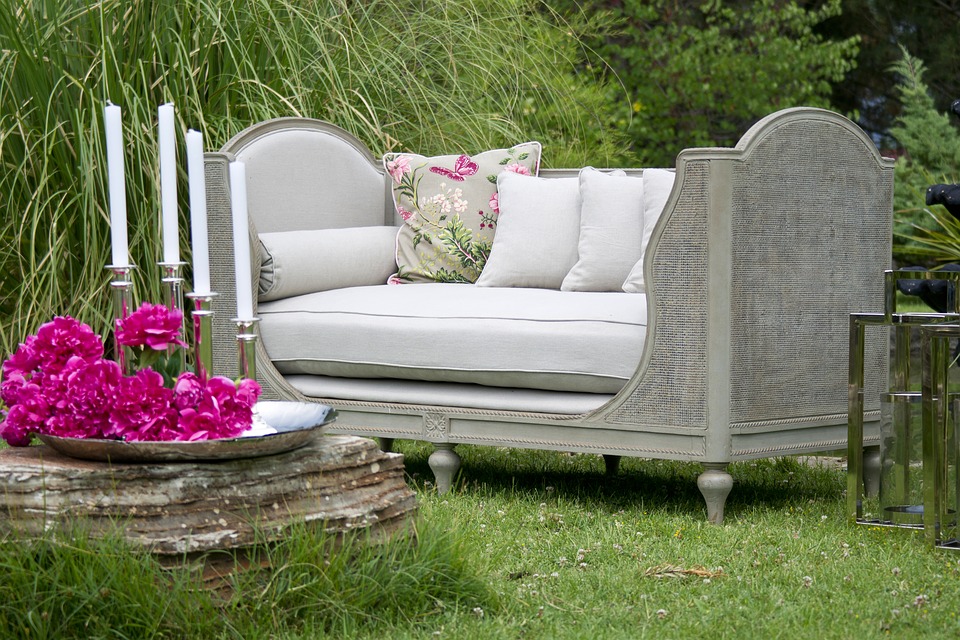 A outdoor couch with flowers and candles in a garden.