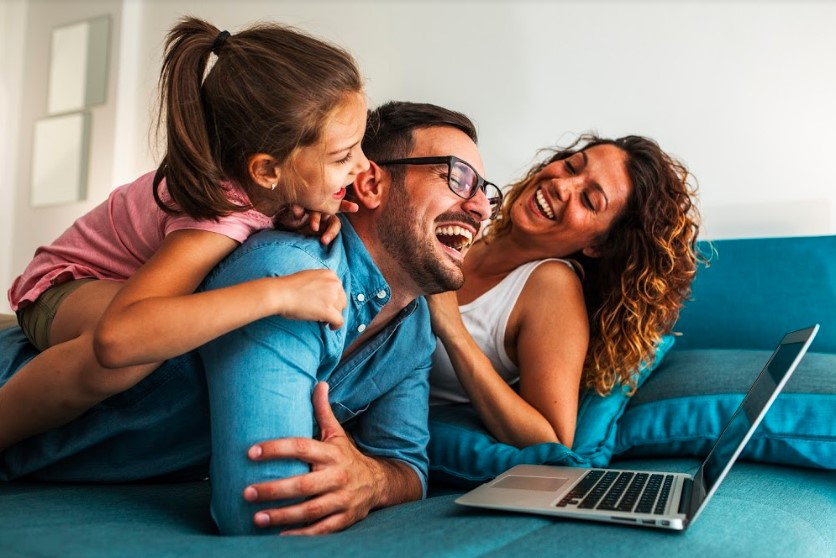 A family is laughing while using a laptop at home to engage in financial planning.