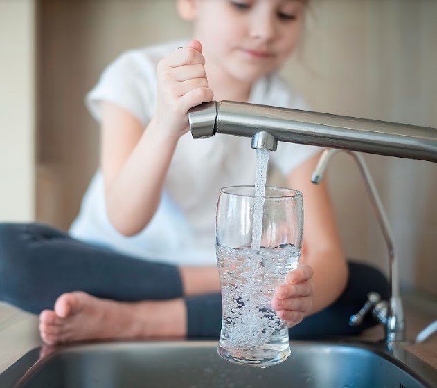 A little girl is filling a glass of safe drinking water from the kitchen sink.