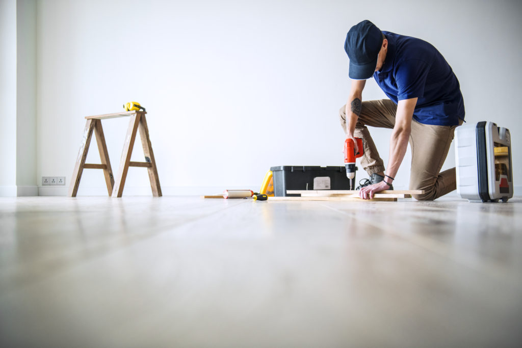 A man is renovating a wooden floor in a room.