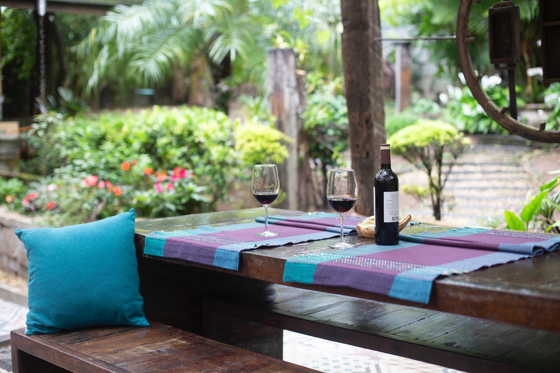 A wooden table with a bottle of wine in a backyard paradise.