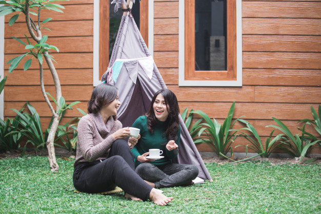 Two women sitting in a teepee in a backyard.