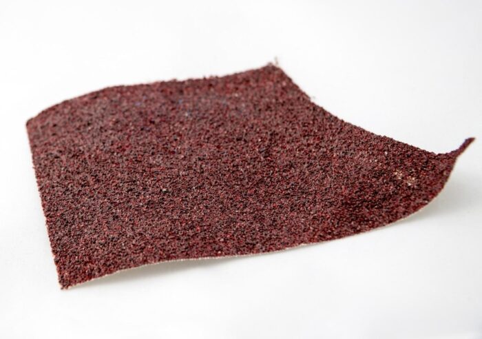 A red sandpaper used with an orbital sander on a white surface.