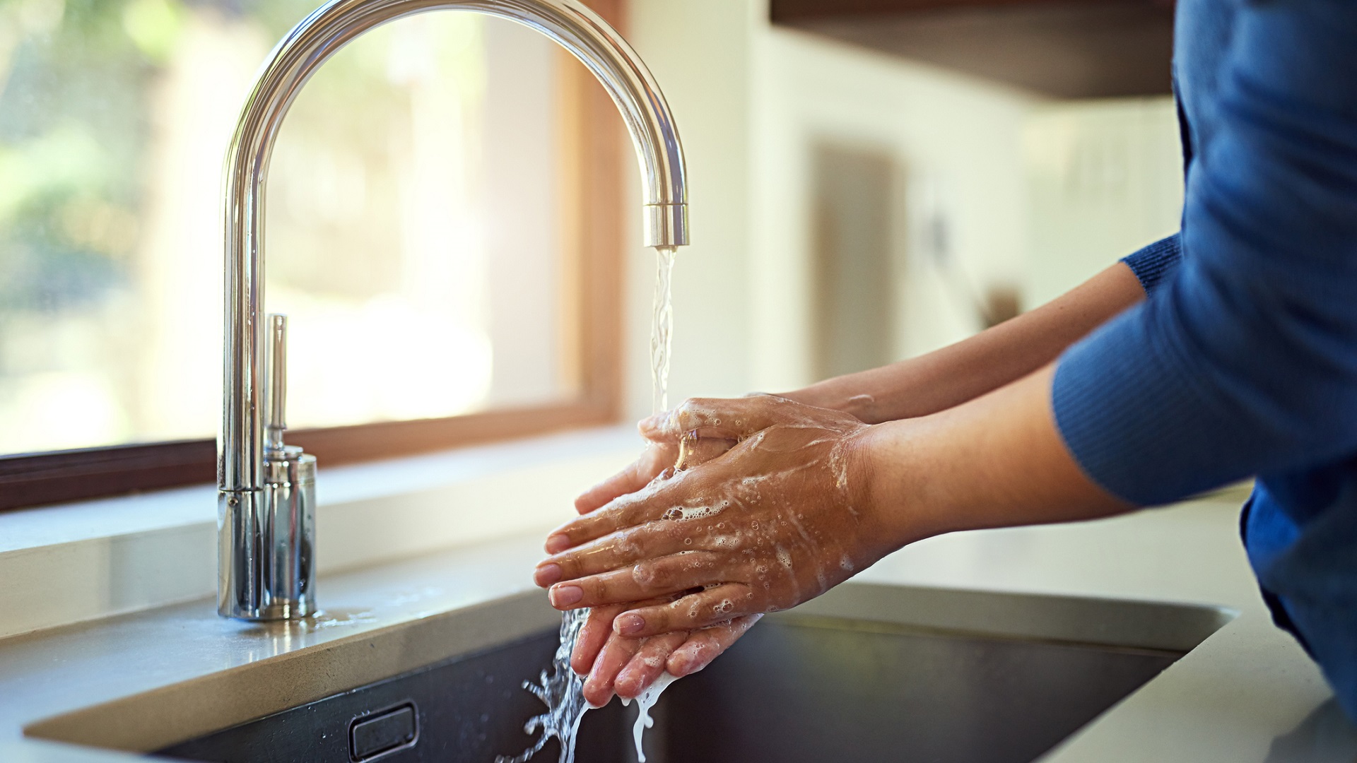 A woman demonstrating effective handwashing technique in a kitchen sink.