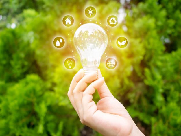 A hand holding a green energy-efficient light bulb with icons.