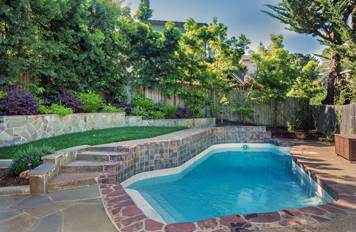 A backyard with a fibreglass swimming pool and landscaping.