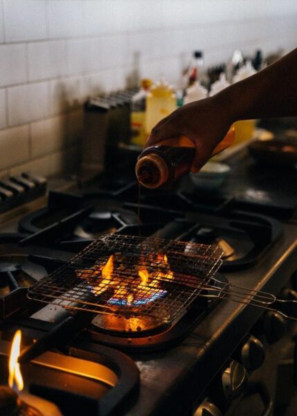 A person performing a grill maintenance by pouring liquid onto a gas heater.