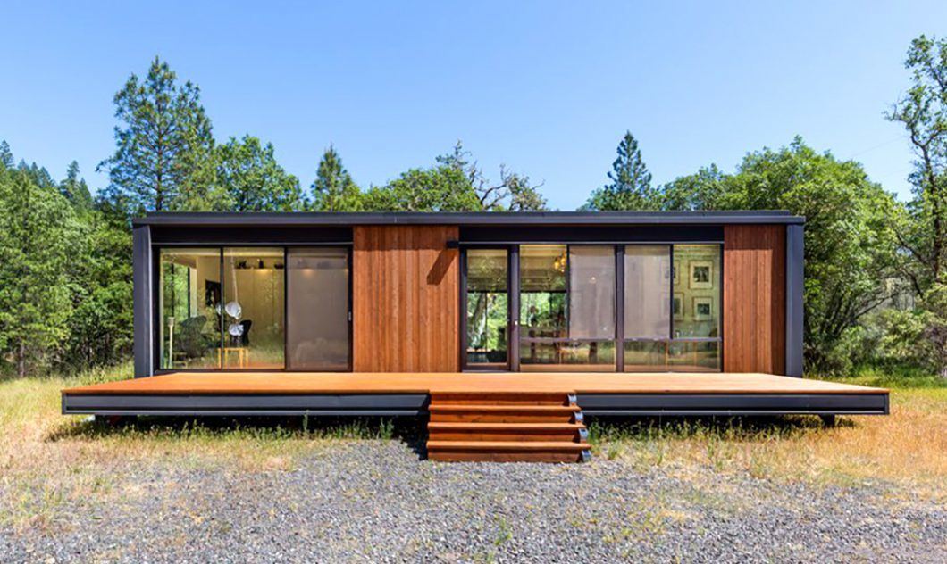 A modern modular home sits in the middle of a wooded area.