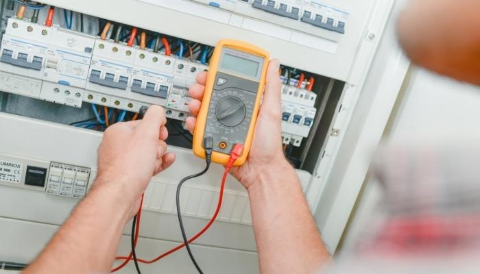 A man using a multimeter to test an electrical panel.