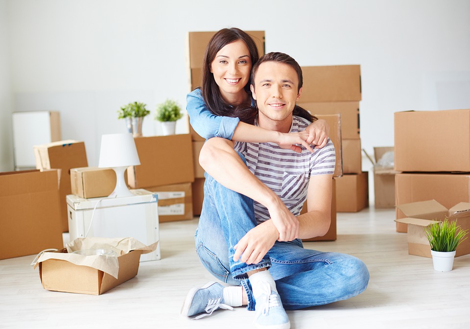 An unmarried couple sitting on the floor in front of moving boxes.