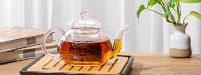 A glass teapot on a wooden tray.