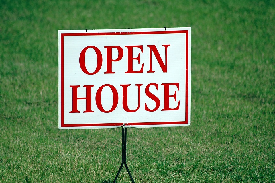 An open house sign for a house on the market for too long displayed in a grassy field.