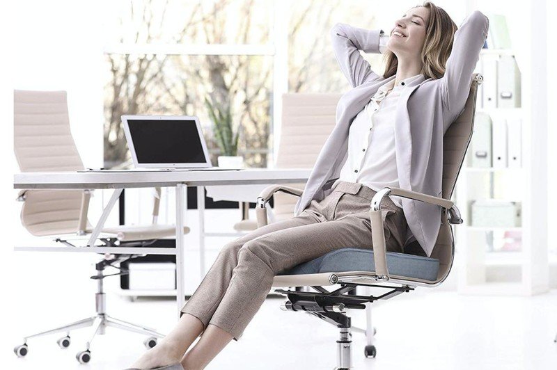 A woman is sitting on a cushioned chair in an office.