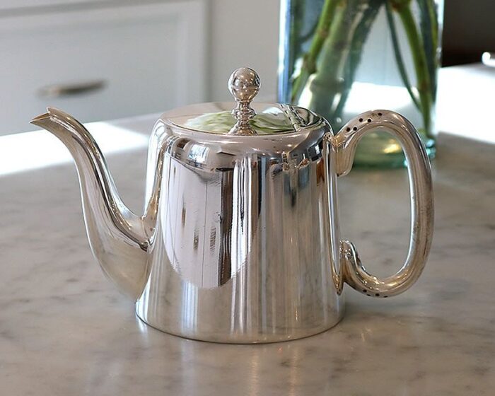 A silver teapot sits on a counter top.