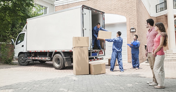 A group of removalists unloading boxes from a moving truck in front of a house.