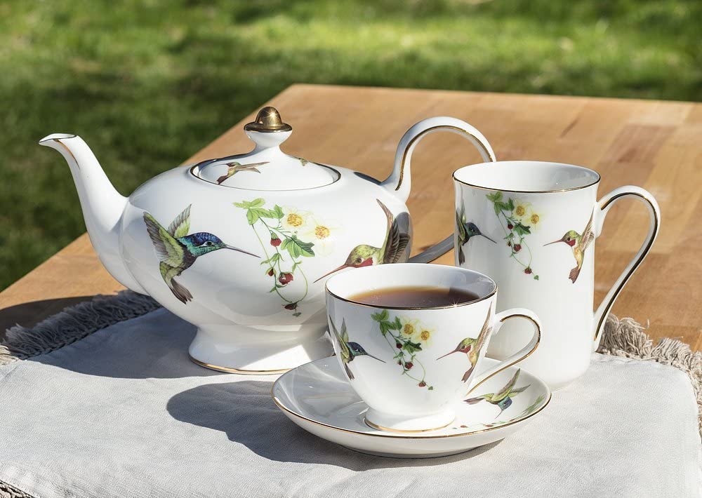 A teapot and cup with hummingbird design on a table.