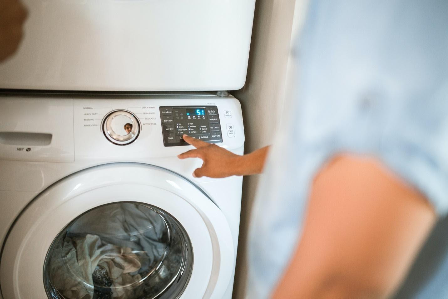 A woman is pointing at a washing machine, indicating factors to consider when choosing one.