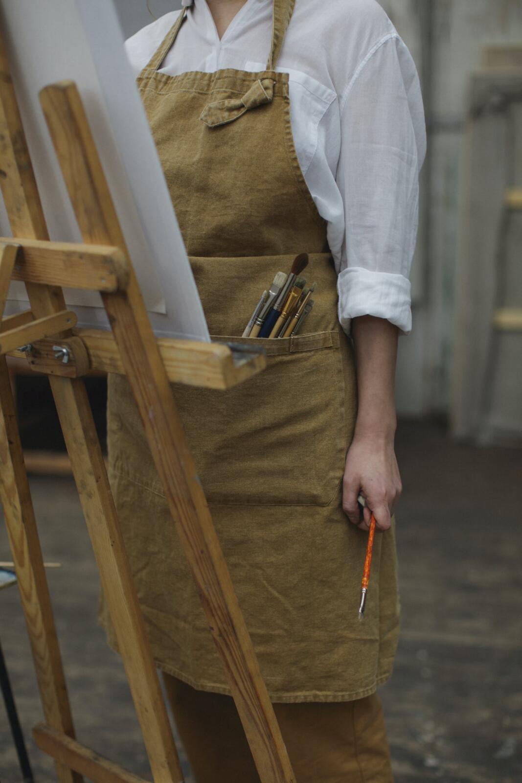 A woman in an apron is painting a portrait on an easel.