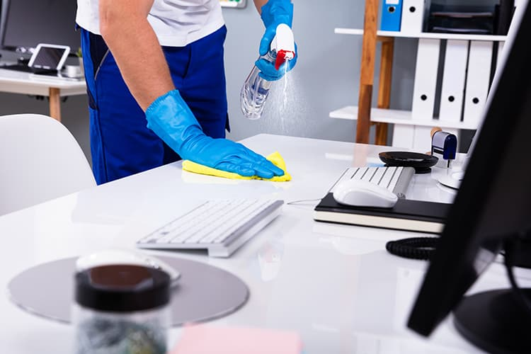 A man in blue gloves tidying an office desk.