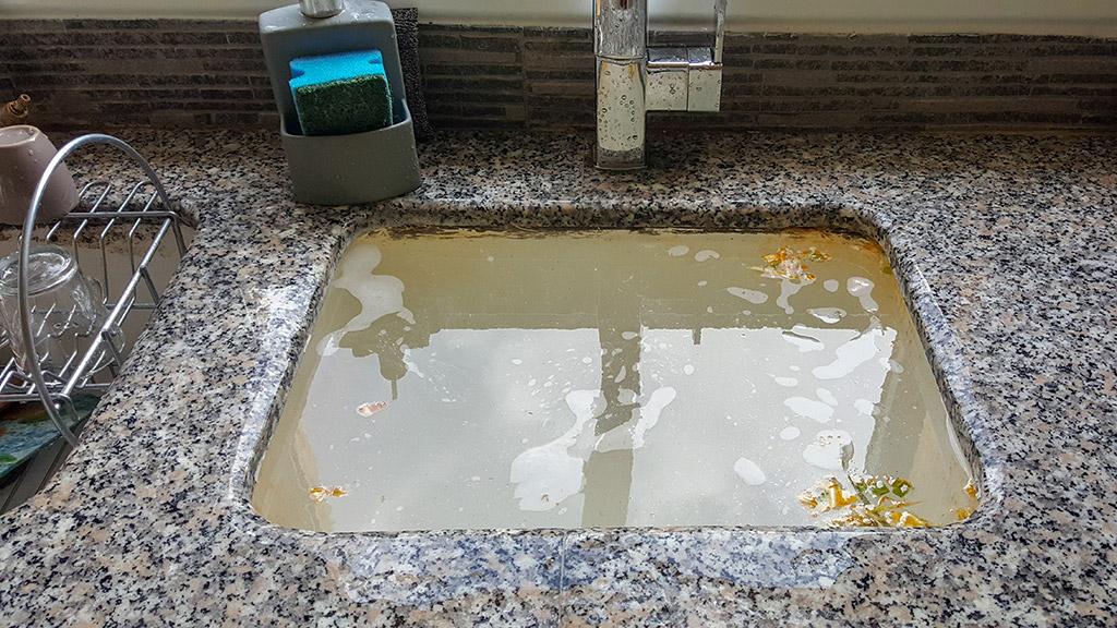 A clogged sink in a kitchen with water in it.