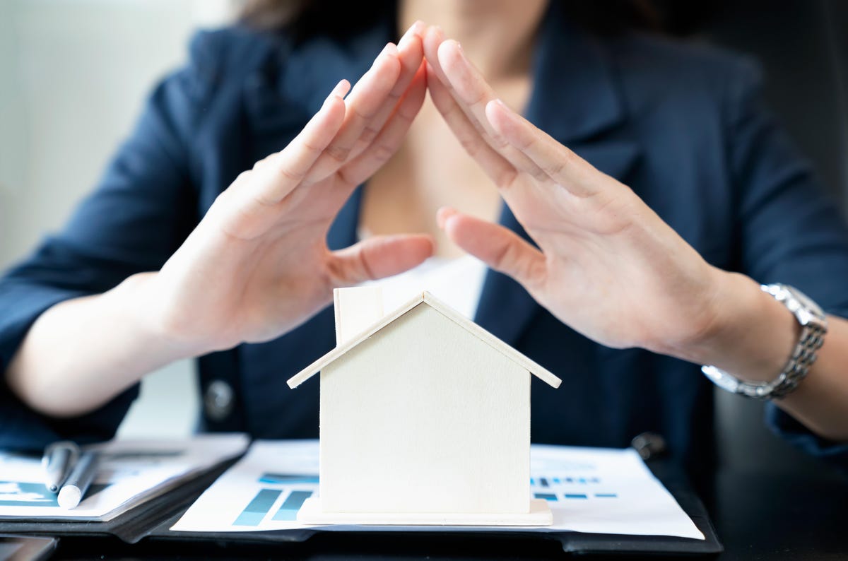 A woman in a business suit is holding a house model in her hands, representing property management.