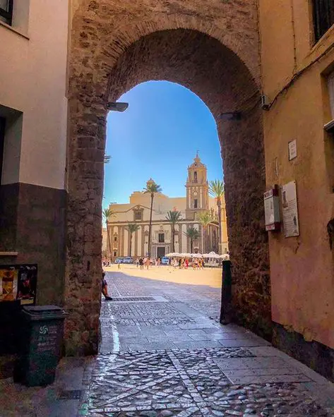 An archway leading to a street with a church in the background showcasing features of Spanish Architecture.