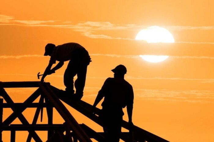 Two construction workers from a roofing company working on a roof at sunset.