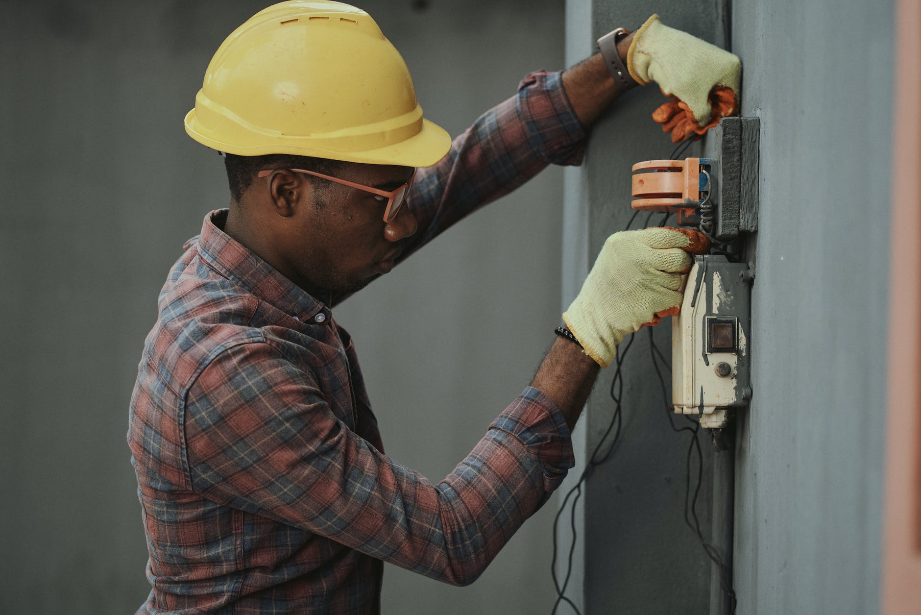 A professional electrician wearing a hard hat is working on an electrical outlet.